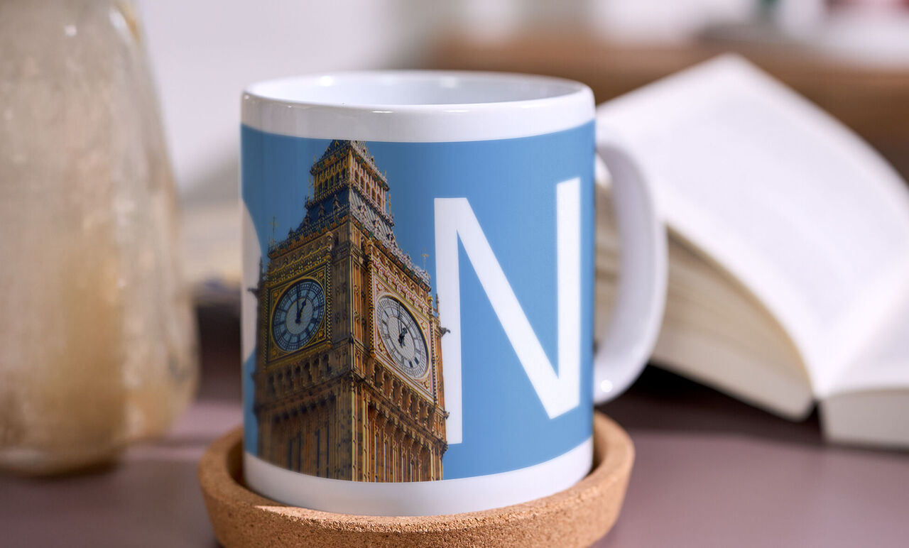 Fotomok met stadsdesignwaarop de klokkentoren Big Ben en de letter N te zien zijn, staat op een onderzetter naast een boek