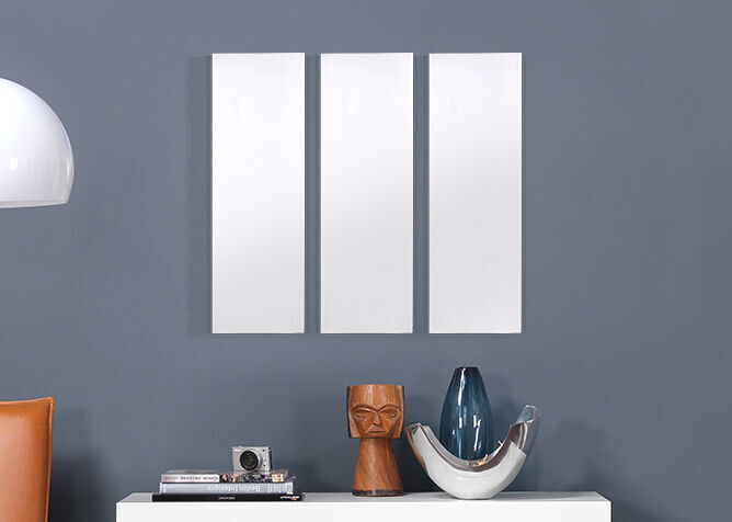 Drie lege, witte fotolijsten aan een grijze muur boven een dressoir met decoratieve objecten.