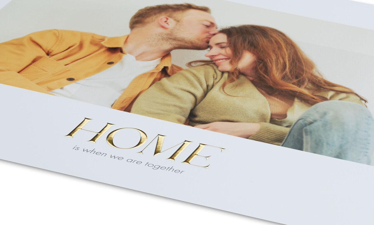 Een paar zit dicht op elkaar op een bank, liefdevol. Op het beeld staat 'HOME is when we are together'.