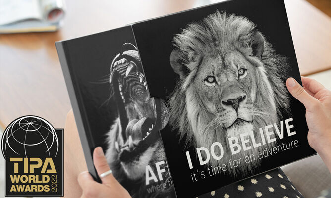 Twee fotoboeken met leeuwenmotieven in de handen van een persoon, een boek benadrukt de zin 'I DO BELIEVE'
