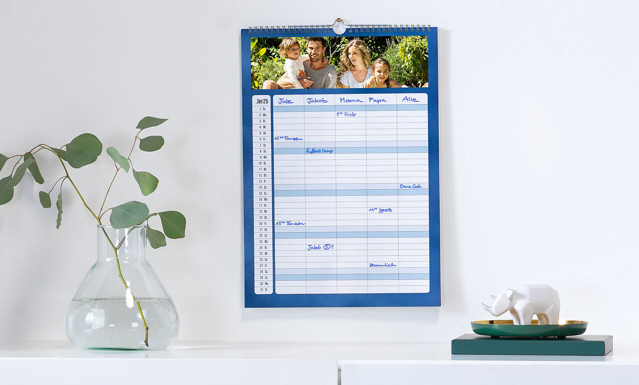 Een blauwe fotokalender hangt aan de muur. Bovenaan een vrolijke gezinsfoto. Onderaan een tabel met ruimte voor notities