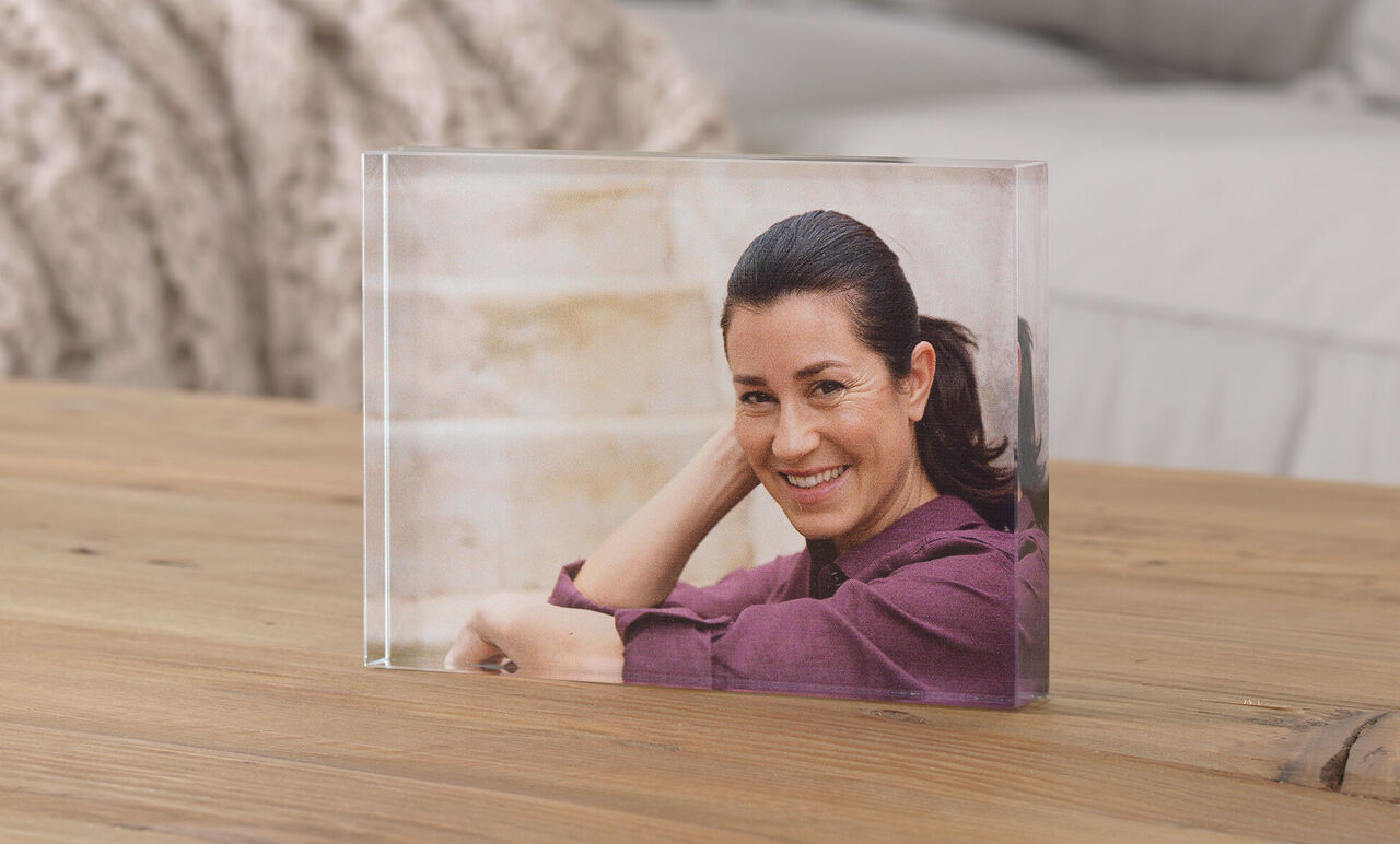 Transparante foto in een blok op een houten tafel, persoon zit ontspannen en glimlacht.