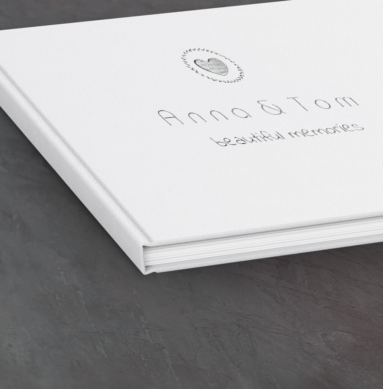 Wit fotoboek met de titel 'Anna & Tom - beautiful memories' op een donkere tafel.
