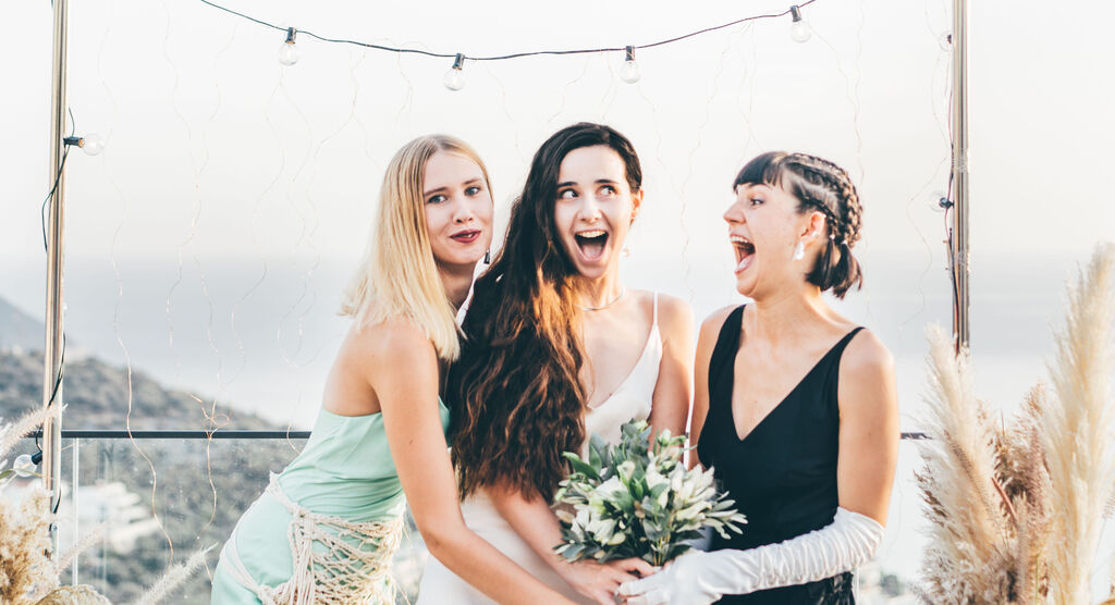 Drie vrouwen in feestkleding omarmen liefdevol en houden een bruidsboeket vast.