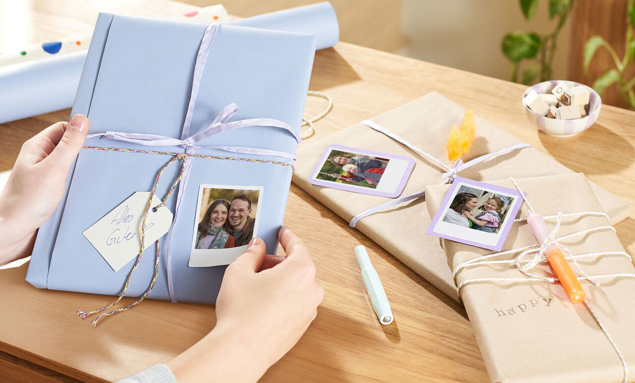 Iemand houdt een creatief verpakt cadeau met Polaroid-foto’s erop. Andere liefdevol ingepakte cadeaus liggen op de tafel.