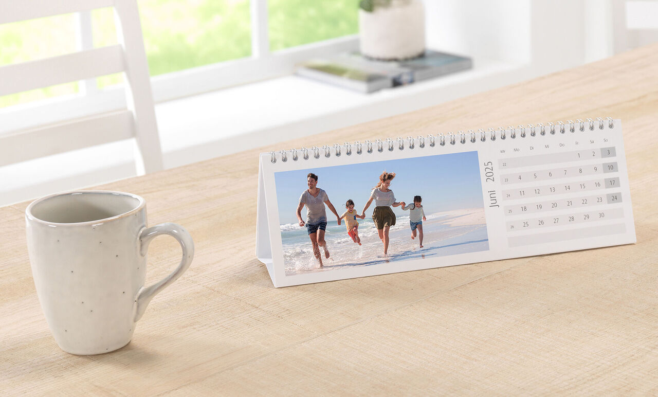 Gezin wandelt op het strand en geniet van de zomer. Een CEWE Fotokalender toont de maand juni.