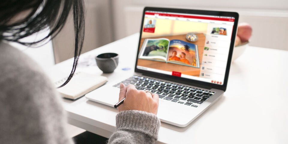 Persoon zit aan tafel met laptop die de CEWE FOTOBUCH website toont.