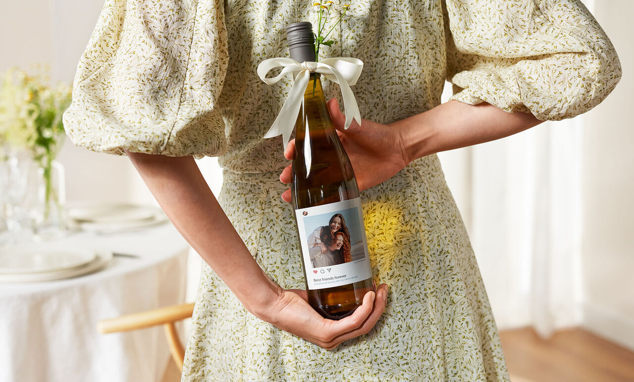 Een persoon houdt een fles wijn met een gepersonaliseerd etiket met een afbeelding en tekst