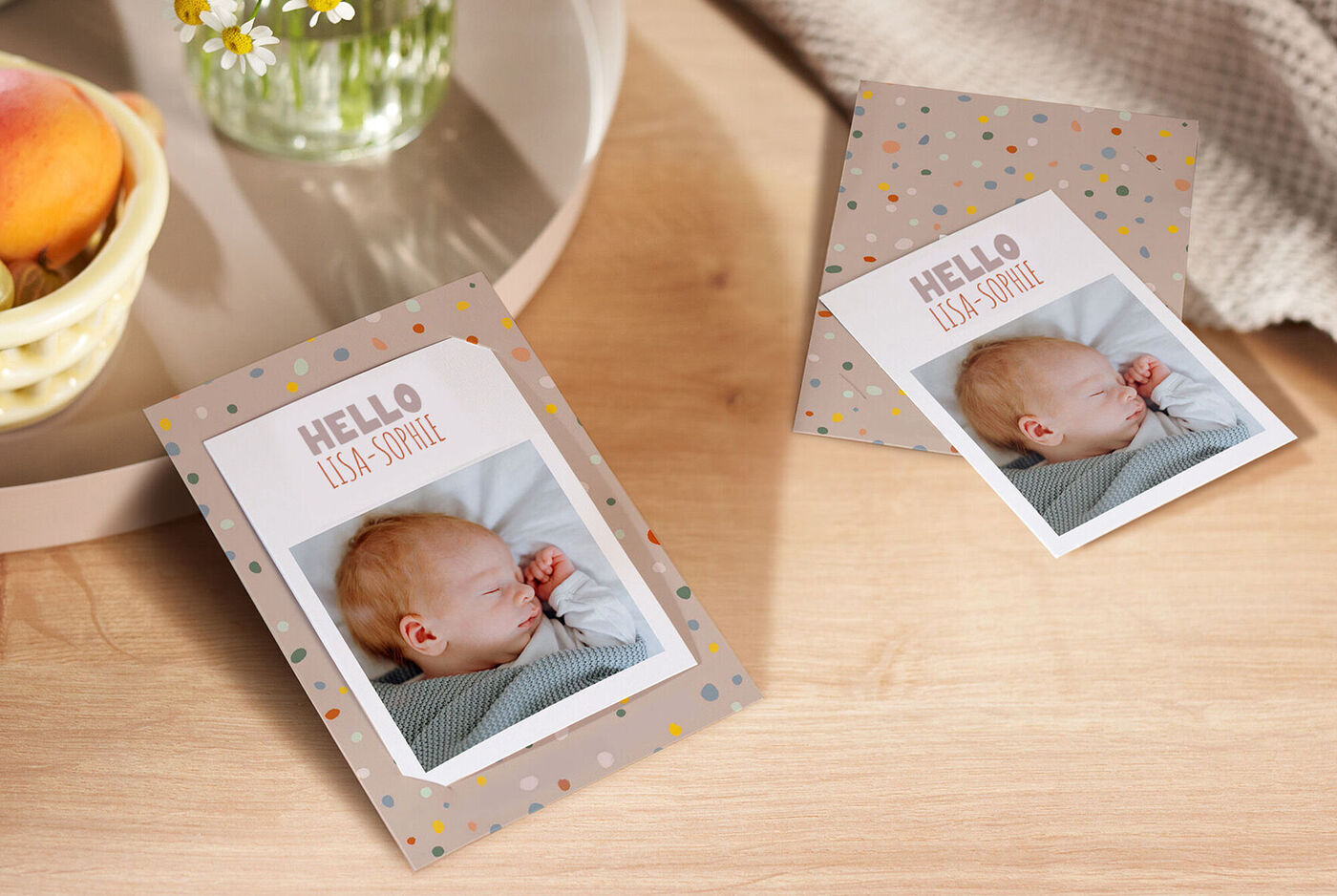 Twee kaarten met foto van slapende baby en de tekst 'Hello Lisa Sophie', omringd door moderne decoratie op tafel