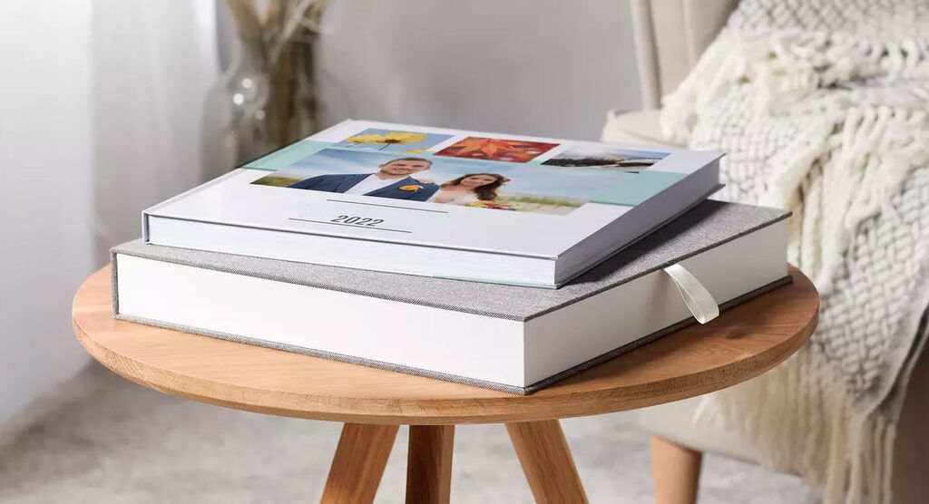 Twee CEWE-fotoboeken op een houten dienblad, één gestapeld en één erop, versierd met favoriete foto's in vrolijke kleuren.