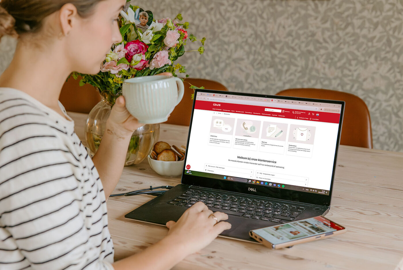 Een persoon zit aan tafel met een laptop en kop.