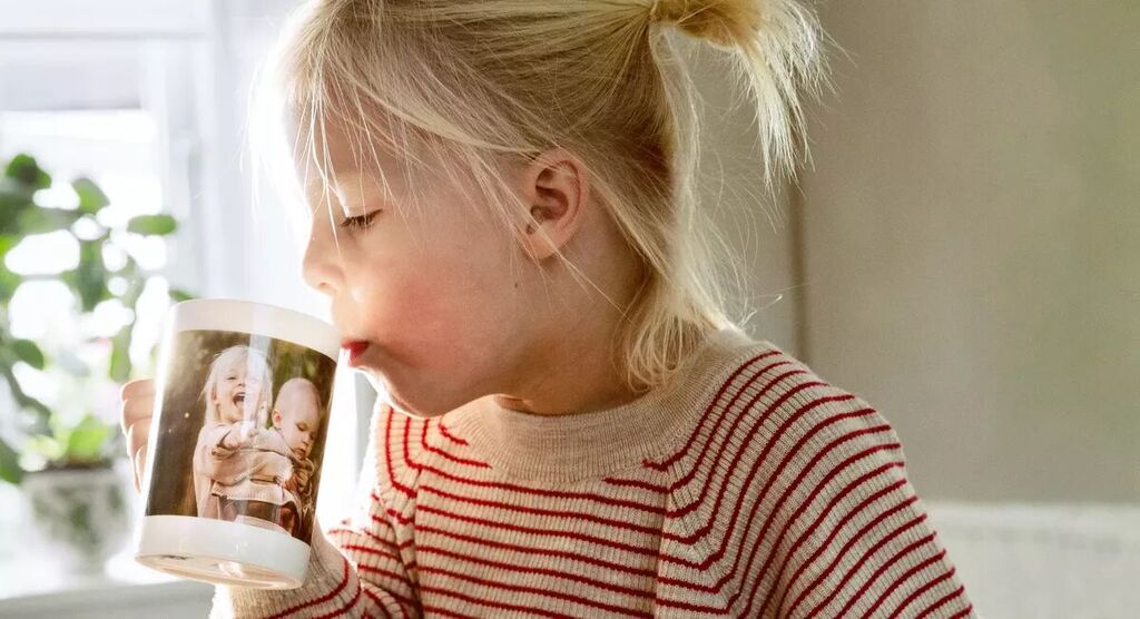 Een kind zit aan tafel met een mok met foto, omgeven door planten.