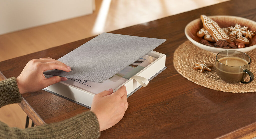 Een persoon bladert door een CEWE fotoboek op een houten tafel.