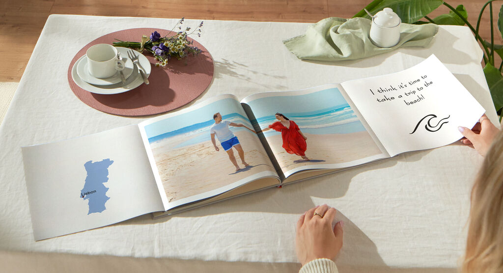 Iemand bladert in een open fotoboek op een tafel met thee en bloemen.