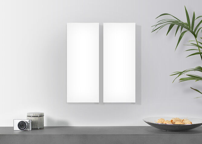 Twee lege witte fotolijsten aan een muur, planten en decoratieborden op de achtergrond.