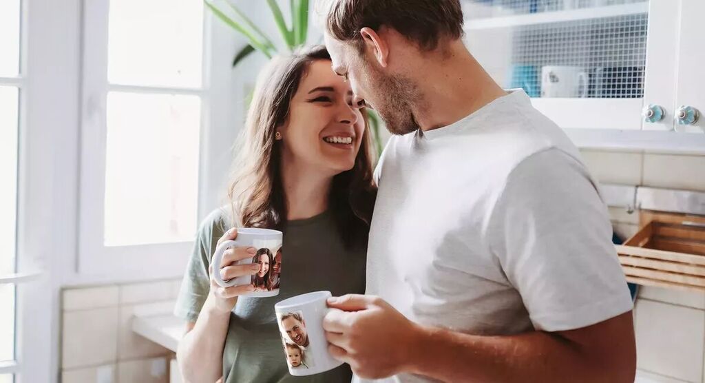 Een koppel geniet van koffie uit gepersonaliseerde mokken in een lichte keuken.