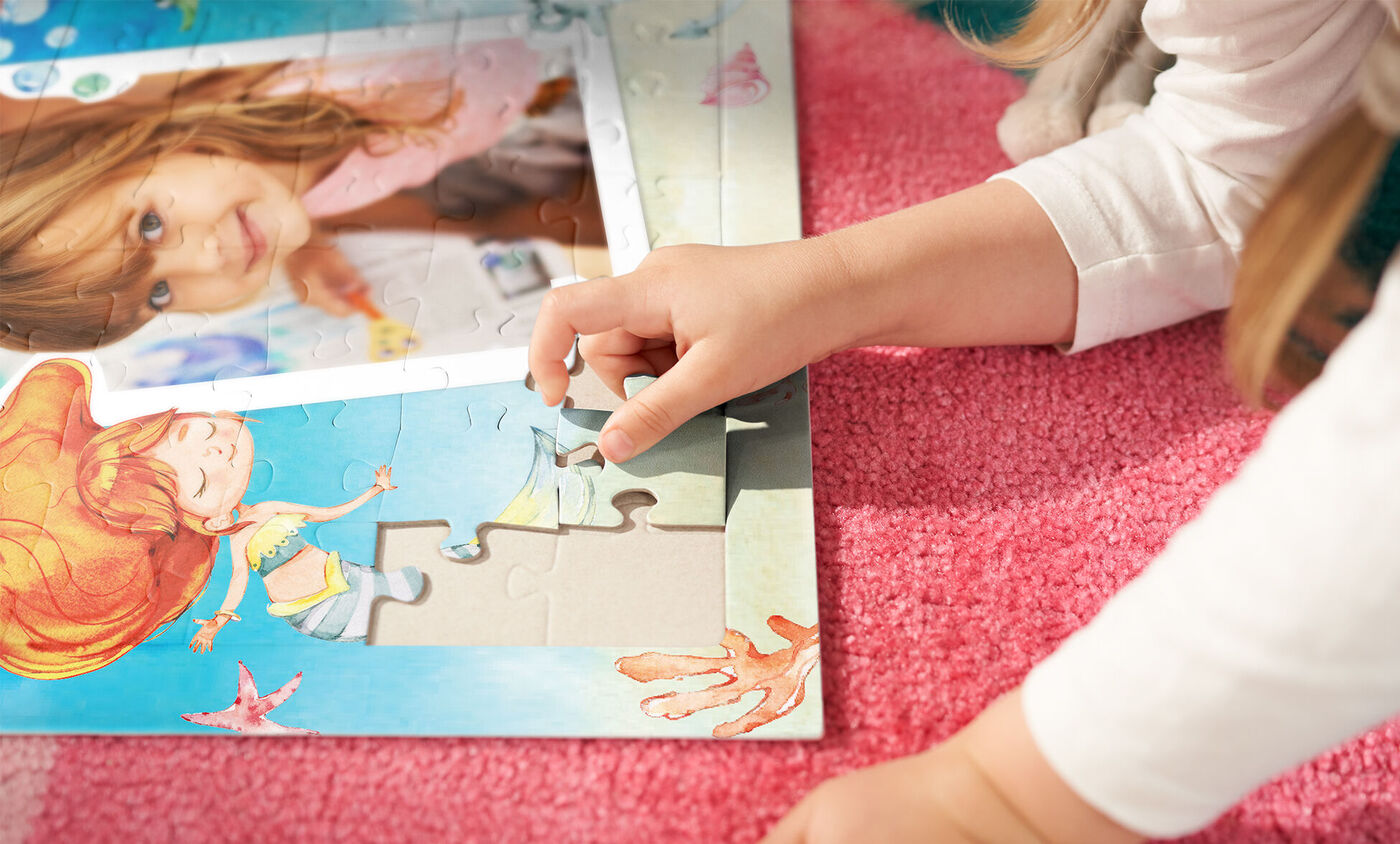 Een kind ligt op een roze tapijt en plaatst een puzzelstukje in een kleurrijke puzzel met vrolijke zeewezens.