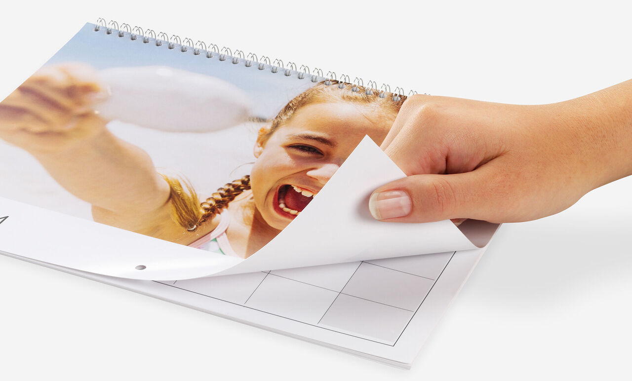 Een hand bladert door een fotokalender, vrolijke vakantiefoto's zichtbaar