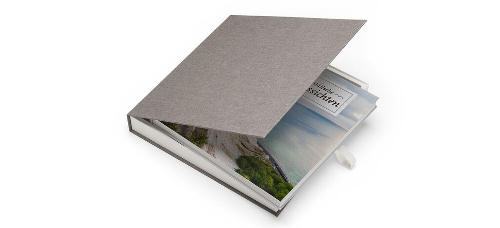 Een liefdevol ontworpen CEWE FOTBOEK met een grijze kaft en open pagina's die een vakantielandschap tonen.