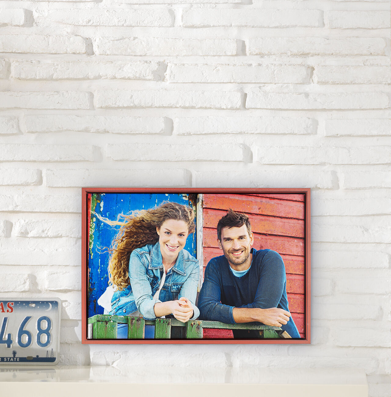Een vrolijk stel leunt tegen een kleurrijk houten hek. De vrouw draagt een spijkerjasje en heeft krullend haar. Achtergrond is rood en blauw.