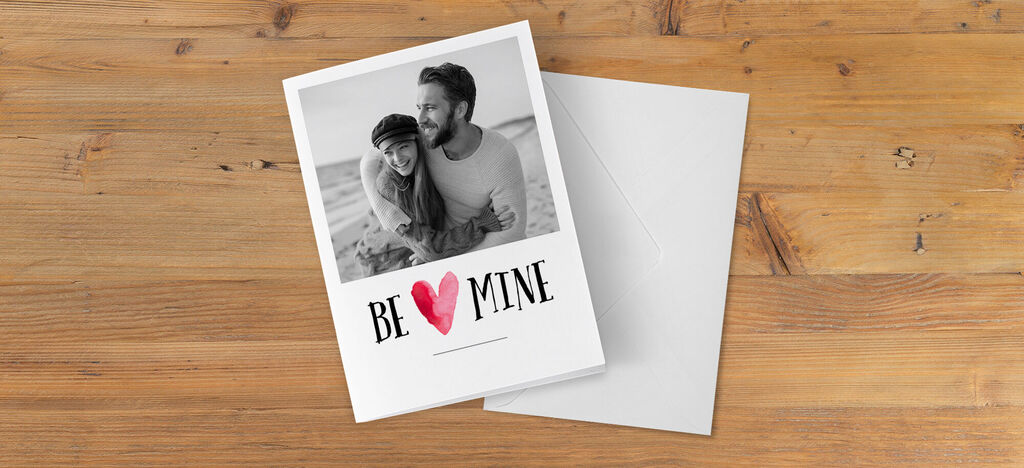 Een romantisch wenskaartontwerp met de tekst 'BE MINE' en een koppel op de voorkant.
