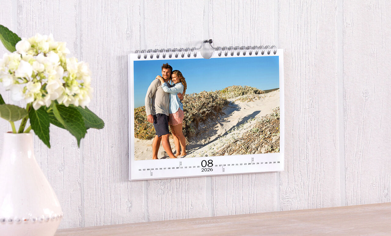 Een mooie wandkalender met een foto van een paar op het strand. De kalender toont augustus 2023.