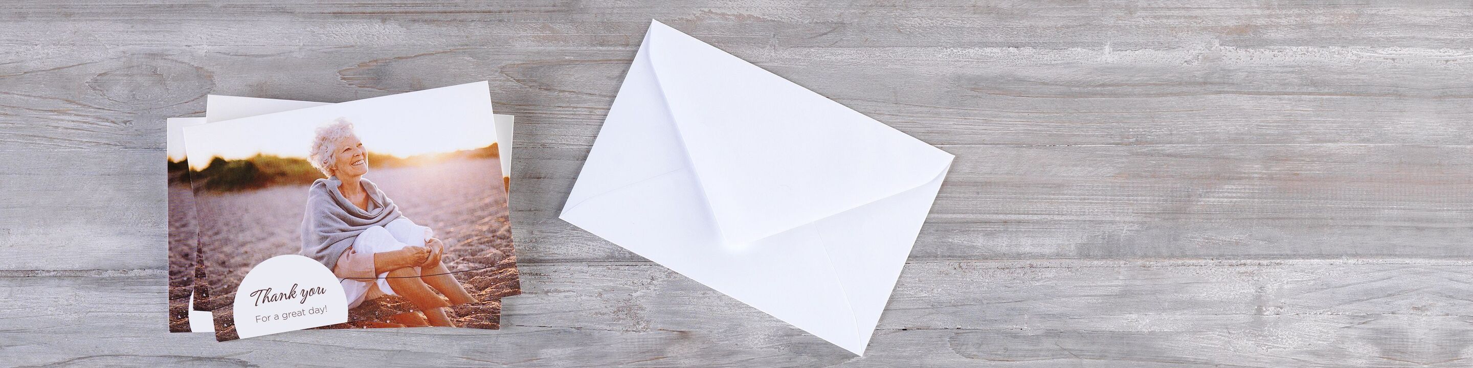 CEWE-wenskaarten met bedanktekst naast een witte envelop op houten oppervlak.