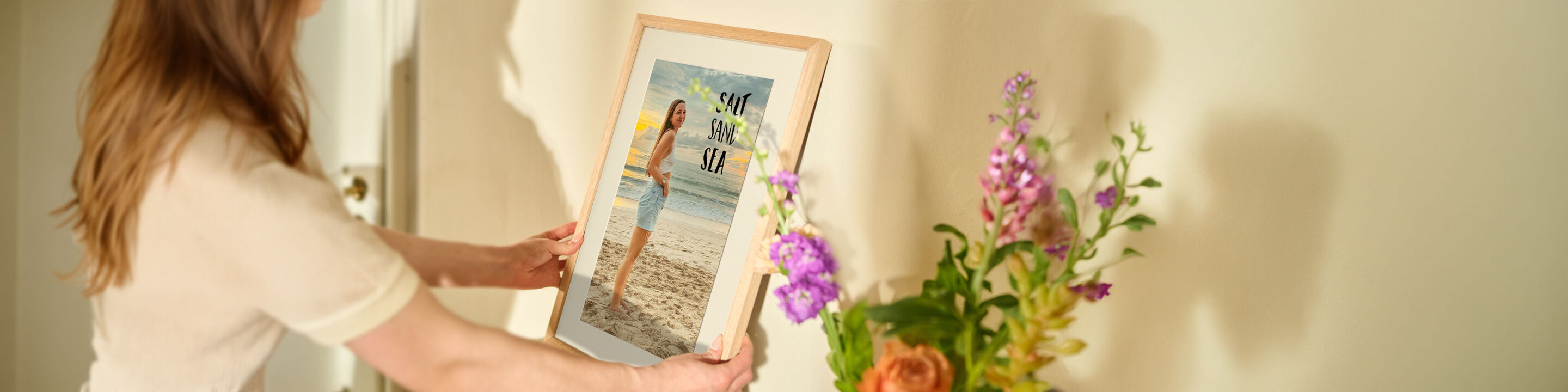Vrouw houdt een wanddecoratie van een vrouw op het strand vast in een mooie houten kader.