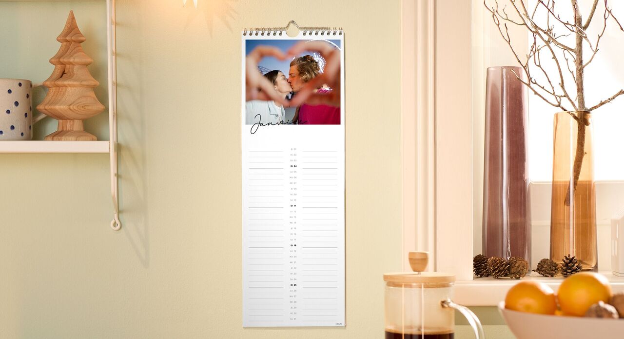 Verjaardagskalender aan een muur met een koppel dat kust door een hart gevormd door hun vingers.
