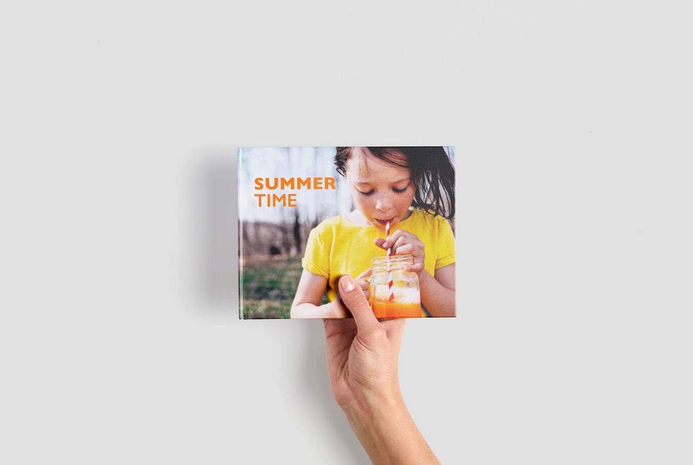 Iemand houdt een CEWE fotoboek vast met een vrolijke zomerfoto op de omslag.