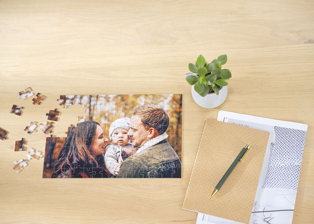 Gepersonaliseerde familiefotopuzzel met ouders en baby op een houten tafel, omringd door losse puzzelstukjes