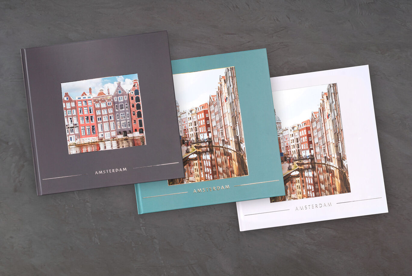 Drie CEWE fotoboeken met afbeeldingen van Amsterdam, elk met een ander kleurenschema.