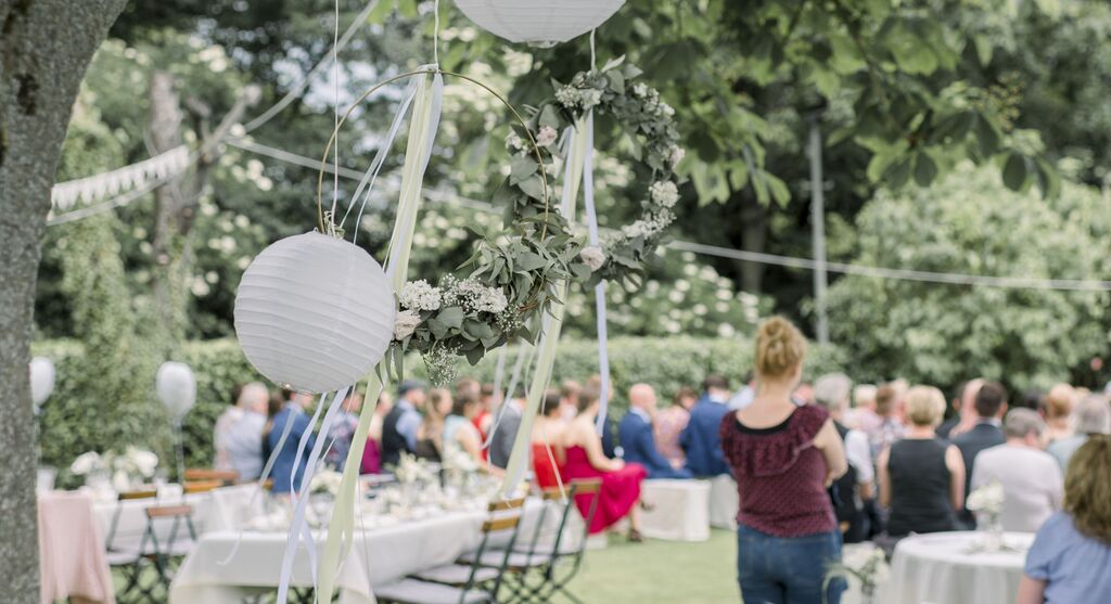 Tuinbruiloft met decoratieve lantaarns en bloemenkrans.