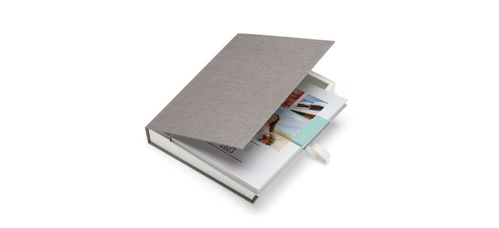 Een geopend CEWE FOTBOEK met kleurrijke foto's en een grijs oppervlak.
