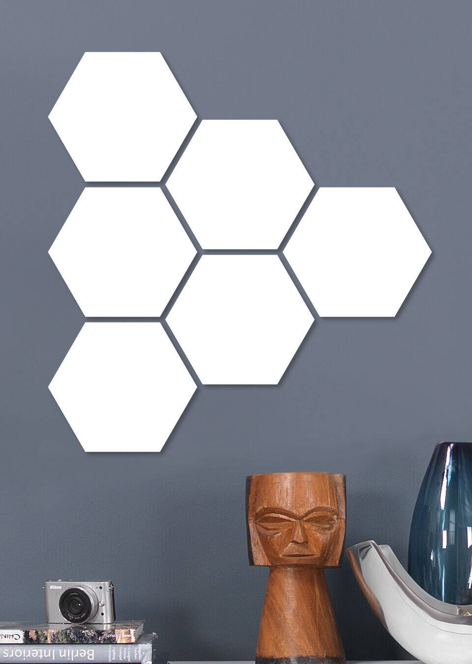 Zes witte hexagonale vormen aan een grijze muur, met een moderne lamp en een camera.