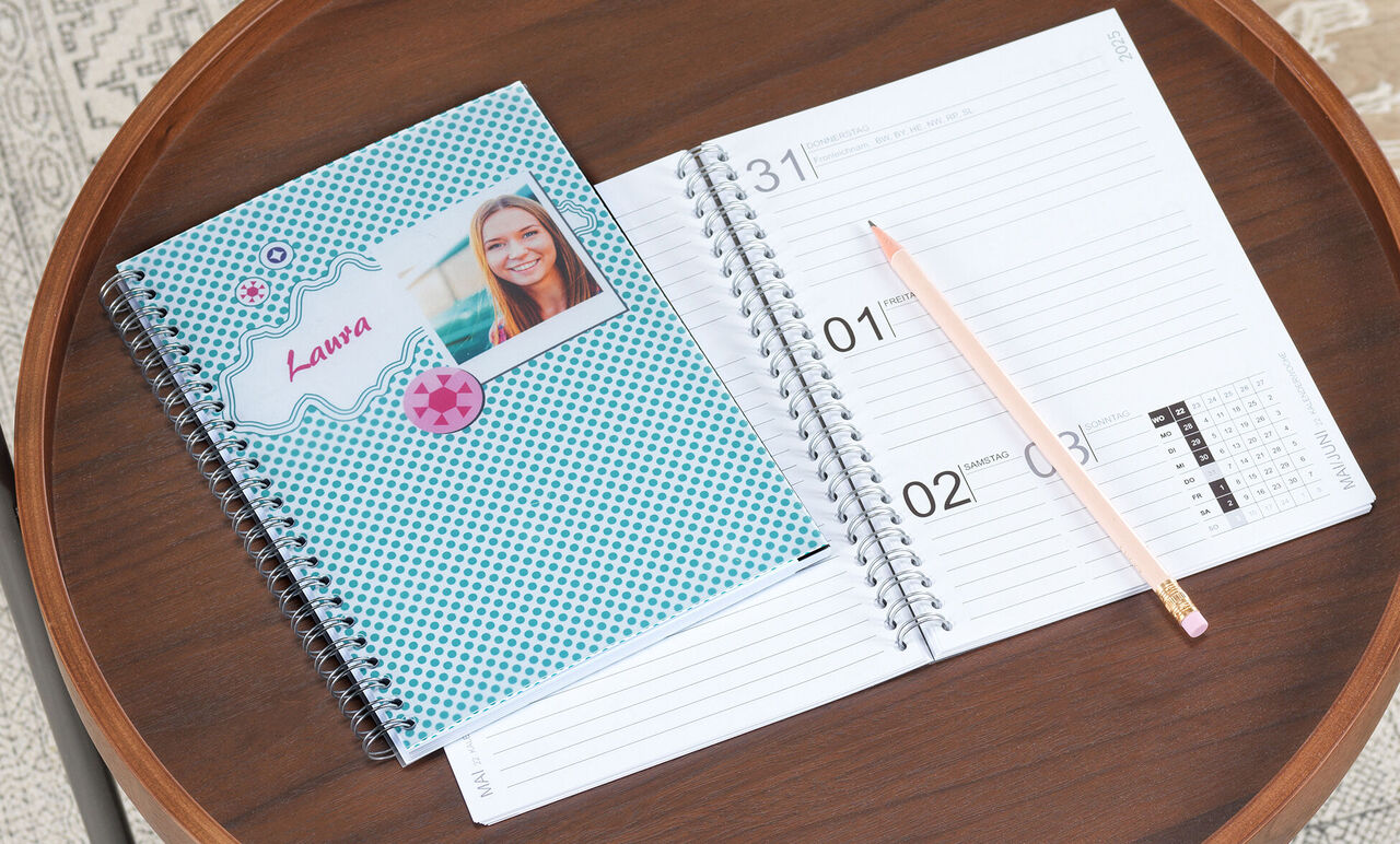 Blauw notitieboek met decoratieve omslag en persoonlijke foto, daarnaast een open kalender en een potlood