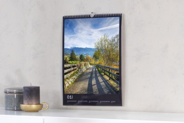 Een prachtige fotokalender aan de muur toont een idyllisch landschap met een pad, omgeven door bomen en bergen.