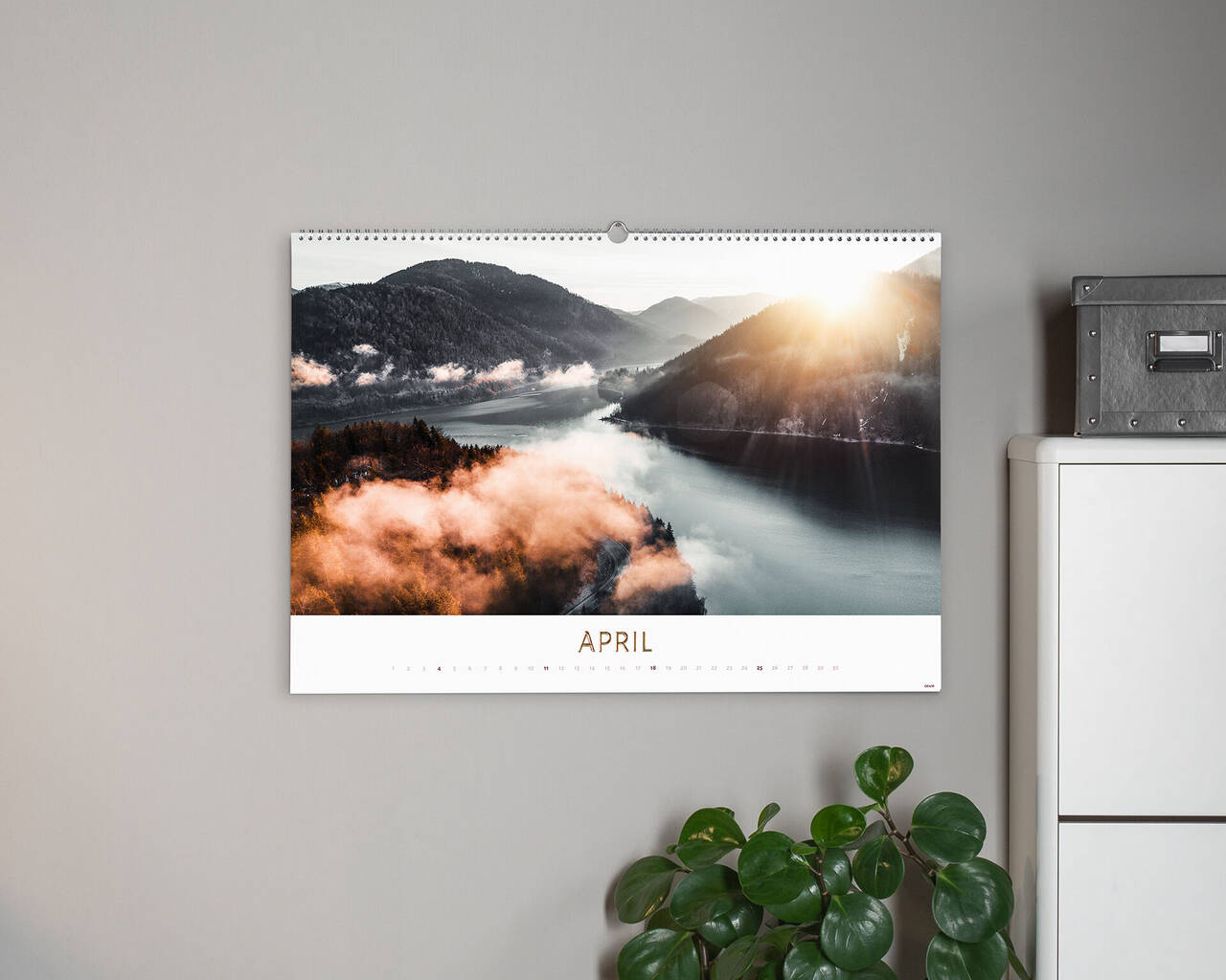 Prachtige fotokalender met een april landschap. Zonsopgang boven mistig meer omgeven door bergen, plant ernaast.