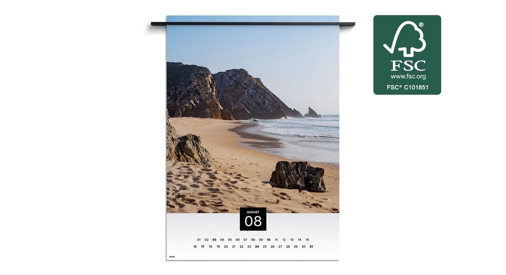 Strandscène met rotsen en zachte golven onder een blauwe hemel in een wandkalender voor augustus.