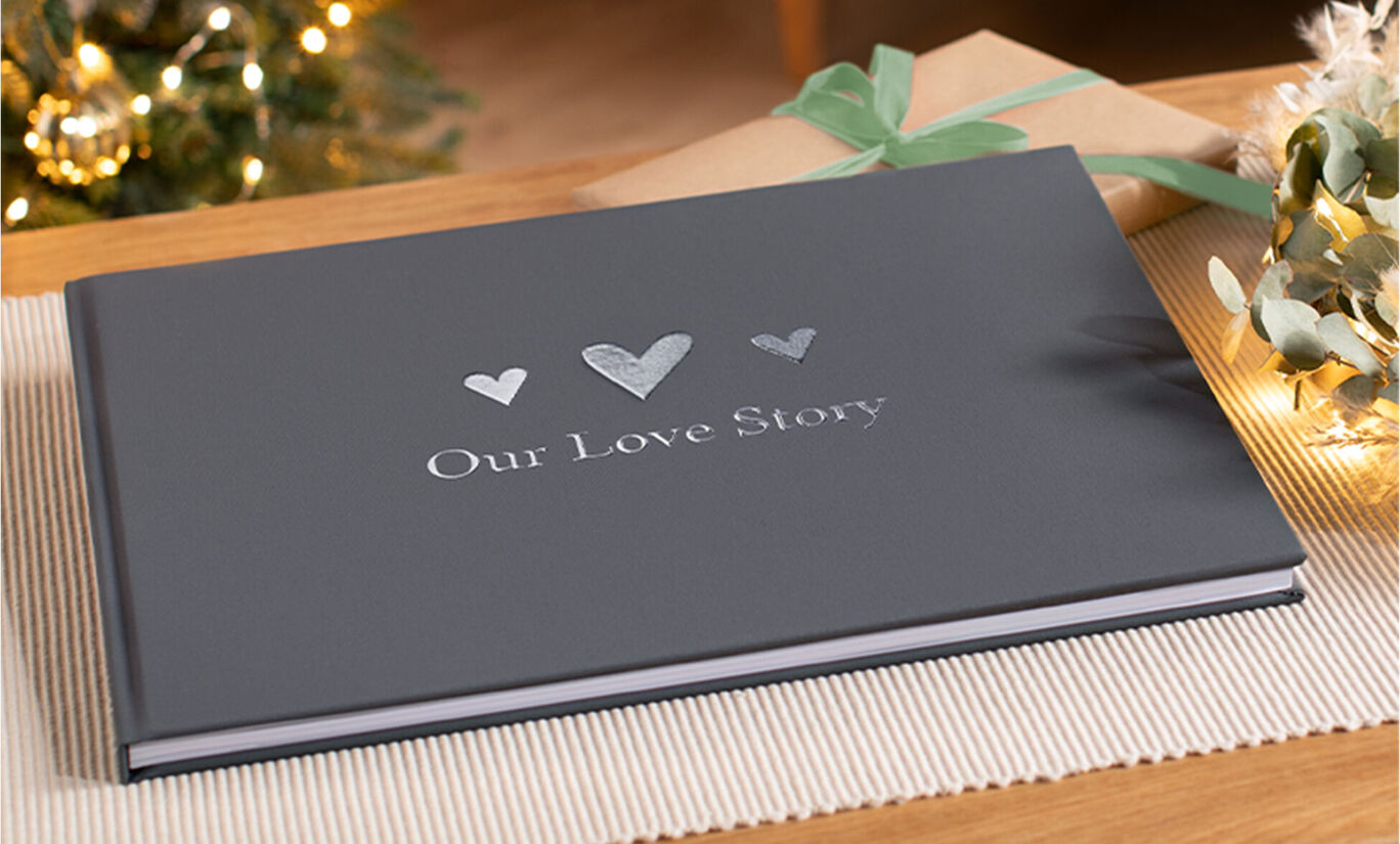 Een mooi CEWE FOTOboek met de titel 'Our Love Story' in een donkergrijze uitvoering op een tafel.