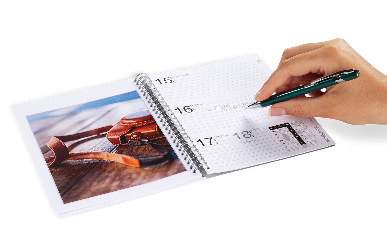 Een hand schrijft in een kalender, daarnaast ligt een foto met zonnebrillen op een tafel.