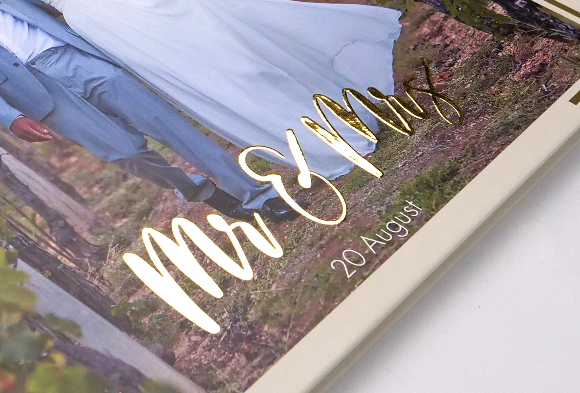 Detailopname van een trouwalbum met de gouden tekst 'Mr & Mrs' en de datum '20 augustus'.
