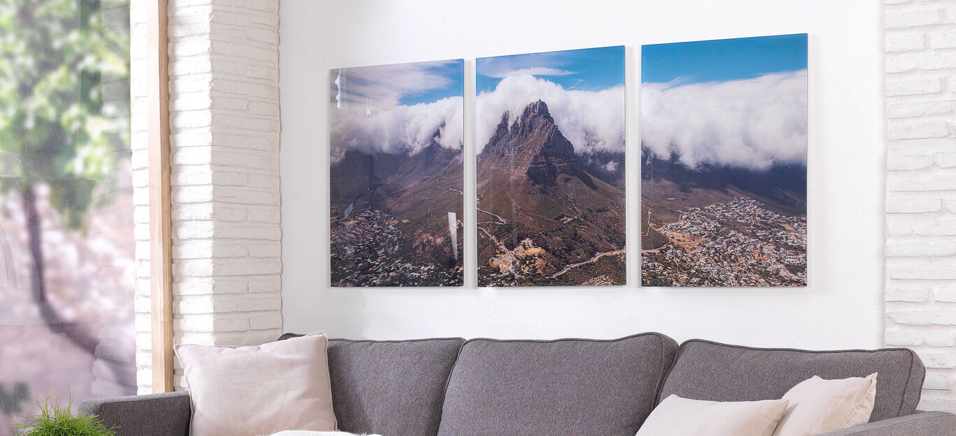 Drie ingelijste landschapsfoto's van een berg met wolken boven de stad.