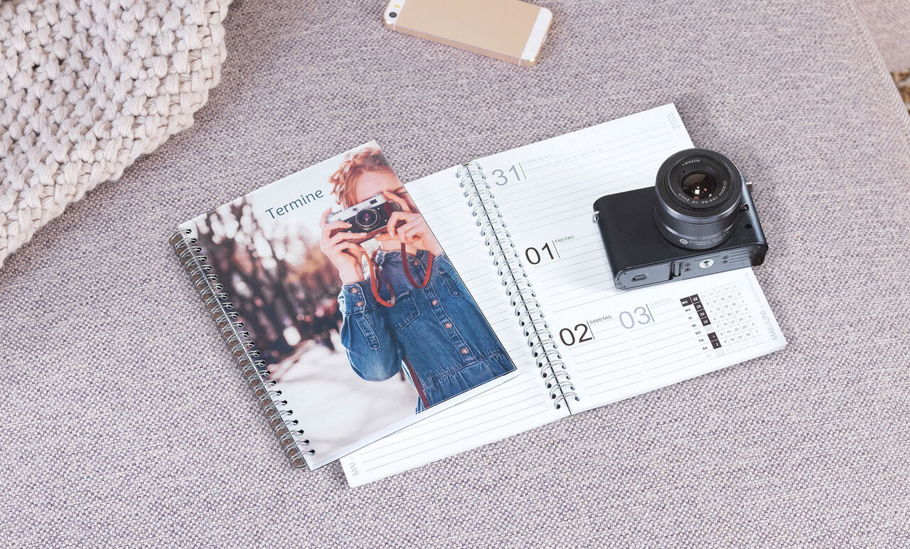 Een open notitieboek met een fotokalender en een camera op een salontafel.