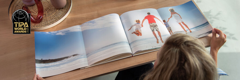 Een persoon bladert door een open fotoboek met strandfoto's van de familie, omgeven door een mooie sfeer.