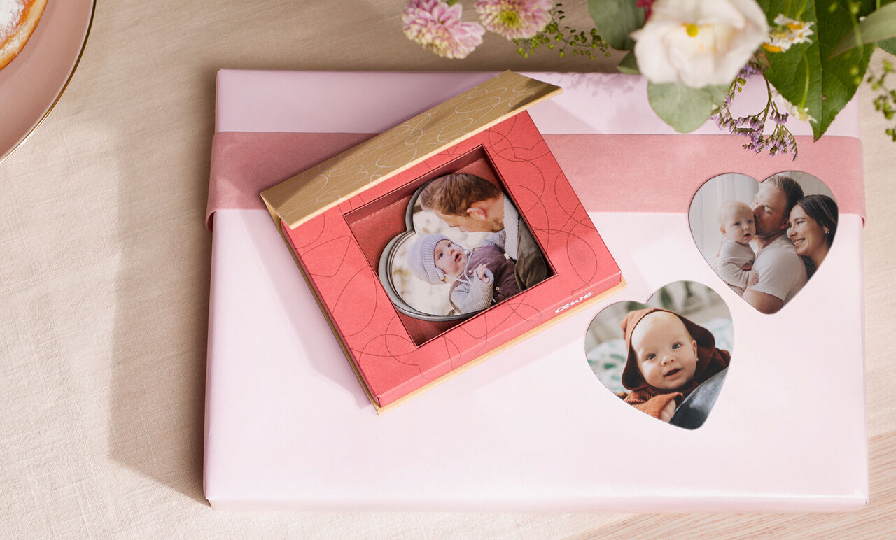 Een mooi rood cadeau met fotokaarten wordt liefdevol gepresenteerd, omringd door bloemen. Perfect om herinneringen te geven.