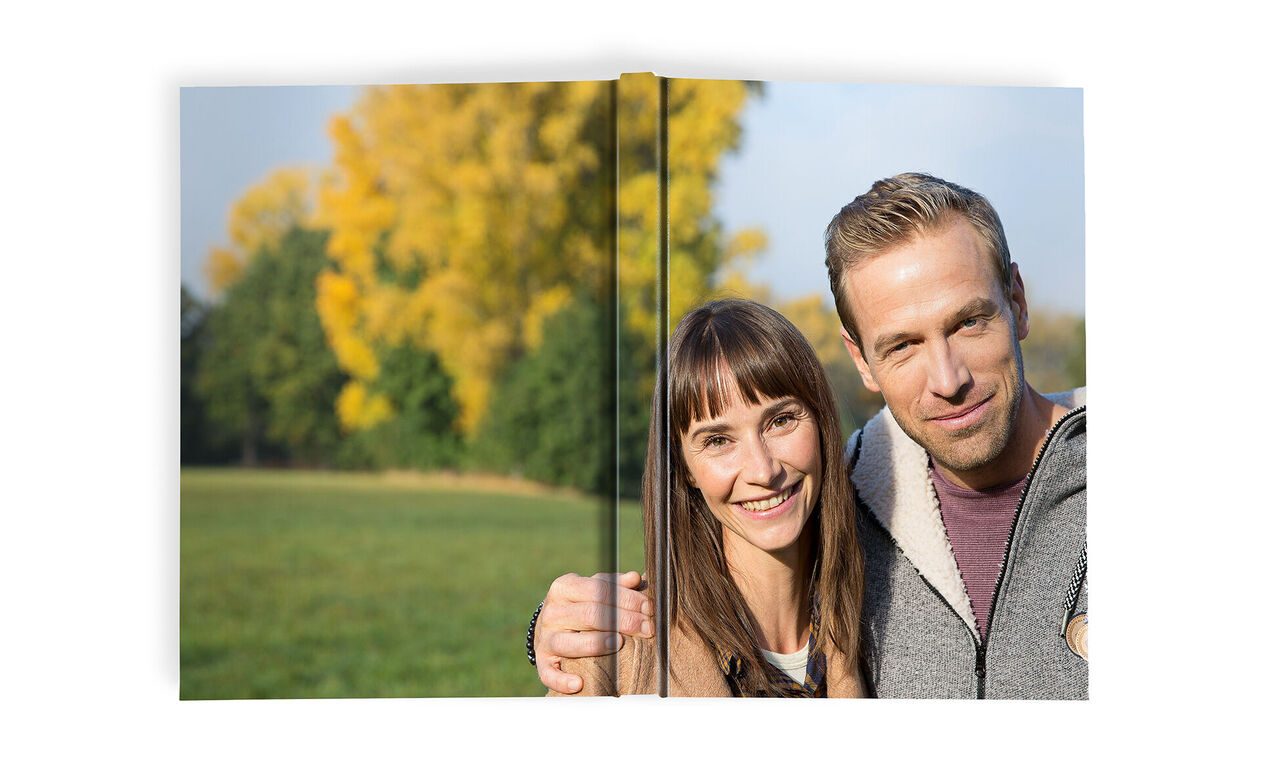 Een koppel houdt een fotoboek vast in een groen park, omringd door herfstbomen.