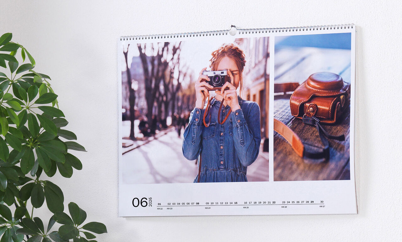 Een wandkalender met een foto van een persoon die fotografeert en een oude camera op een tafel