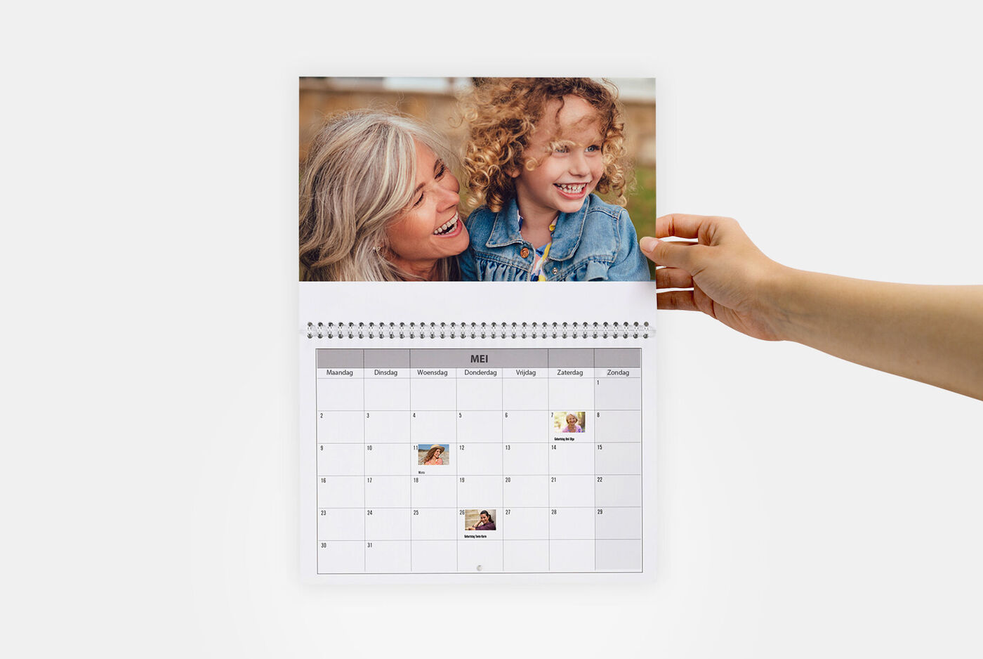 Hand houdt een CEWE fotokalender met familiefoto's. De maand mei met kleine foto-uitsnedes.