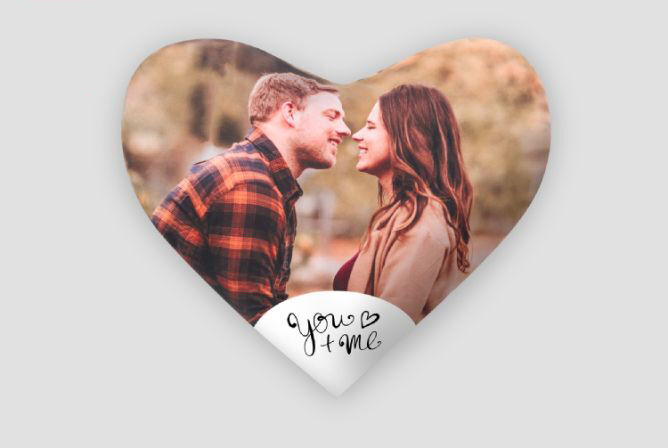 Een stel dat liefdevol zoent in de natuur, omgeven door een hartvormige decoratie met "you + me".